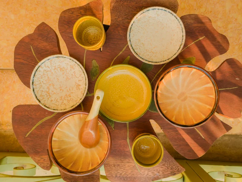An overhead view maps cups, bowls, spoon and plates across a leaf-shaped wooden table