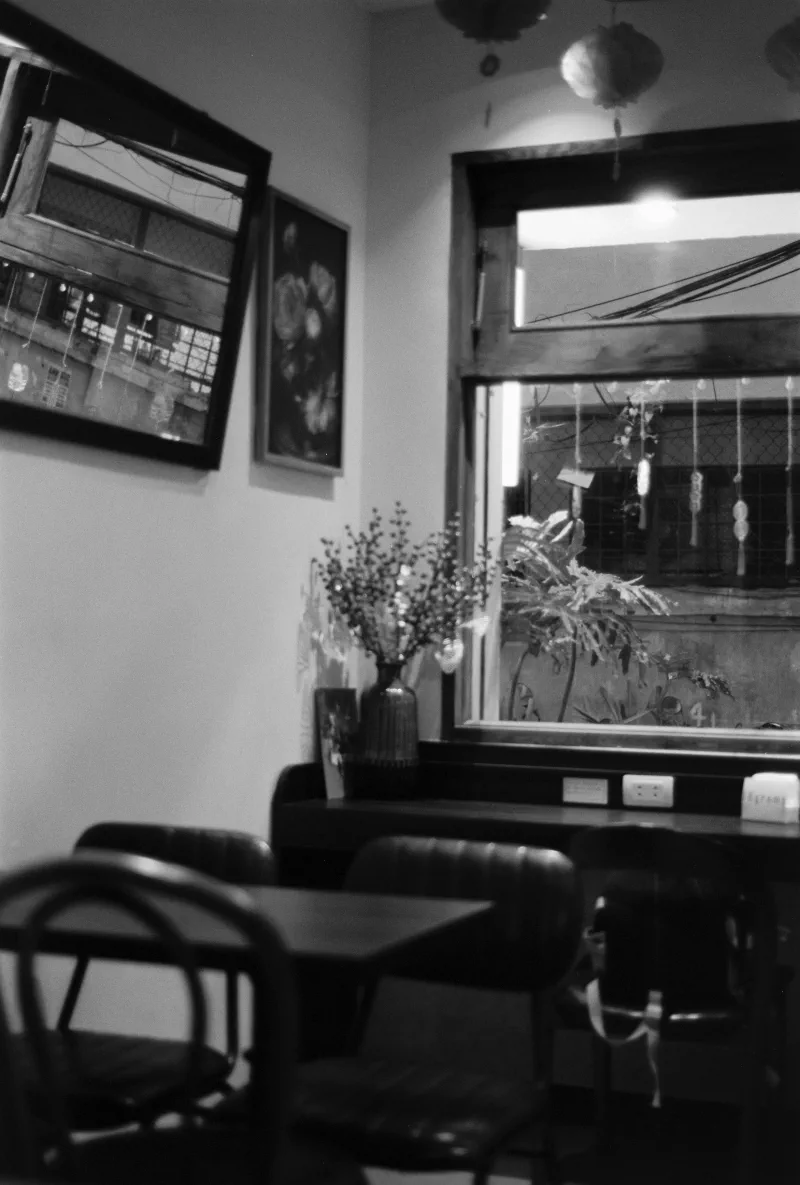 An empty cafe corner holds dark chairs, framed pictures, a vase and paper lanterns