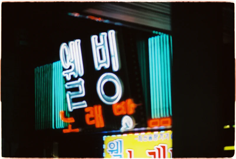 A close view of a Hangul neon sign glowing white, turquoise and orange against black