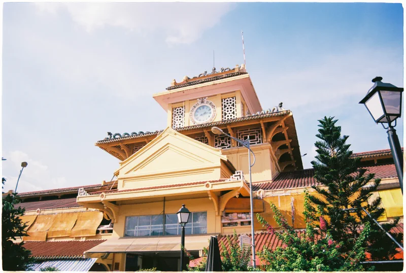 The ochre clock tower and tiled roofs of a Sài Gòn market rise into blue sky