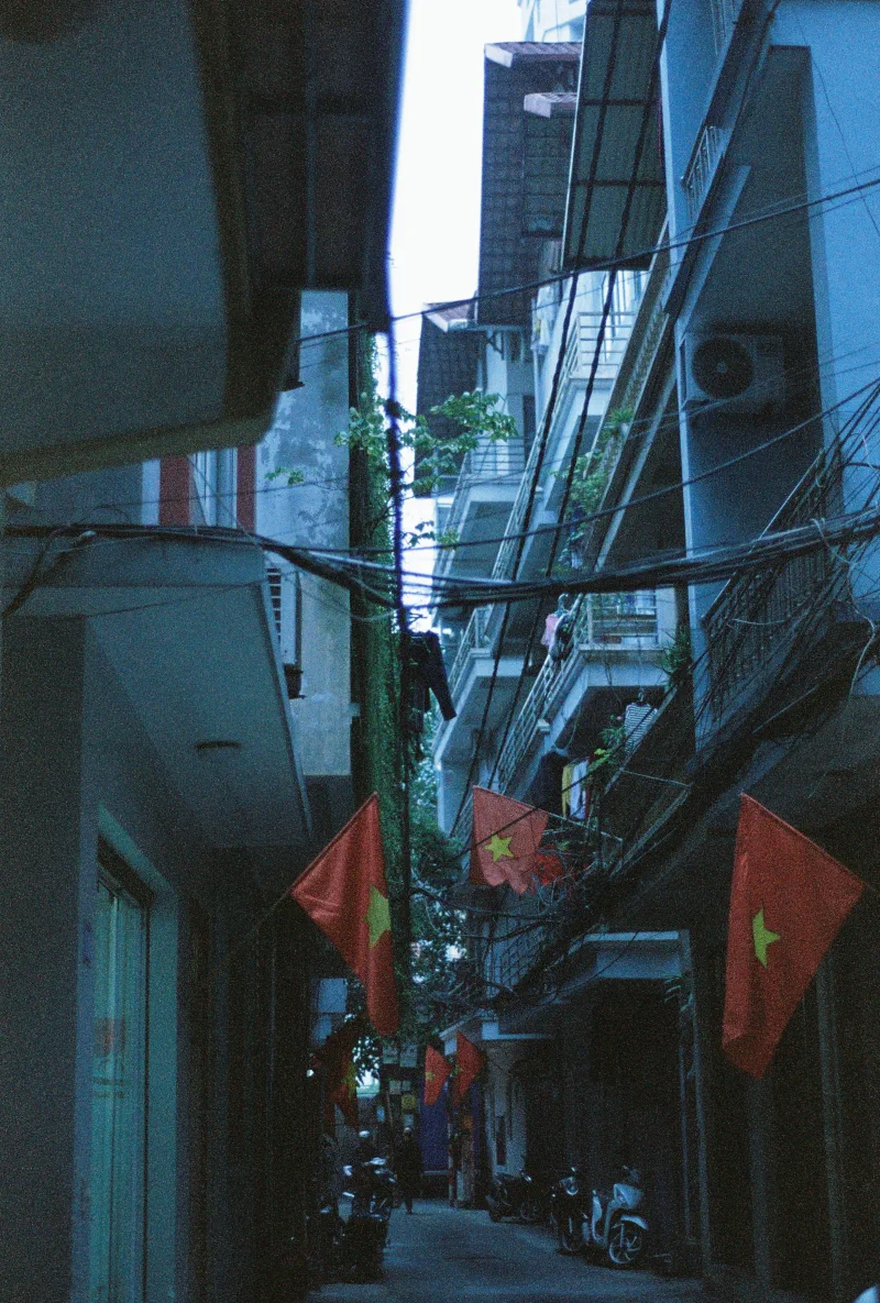 Vietnamese flags repeat through a narrow blue-toned residential alley at dusk