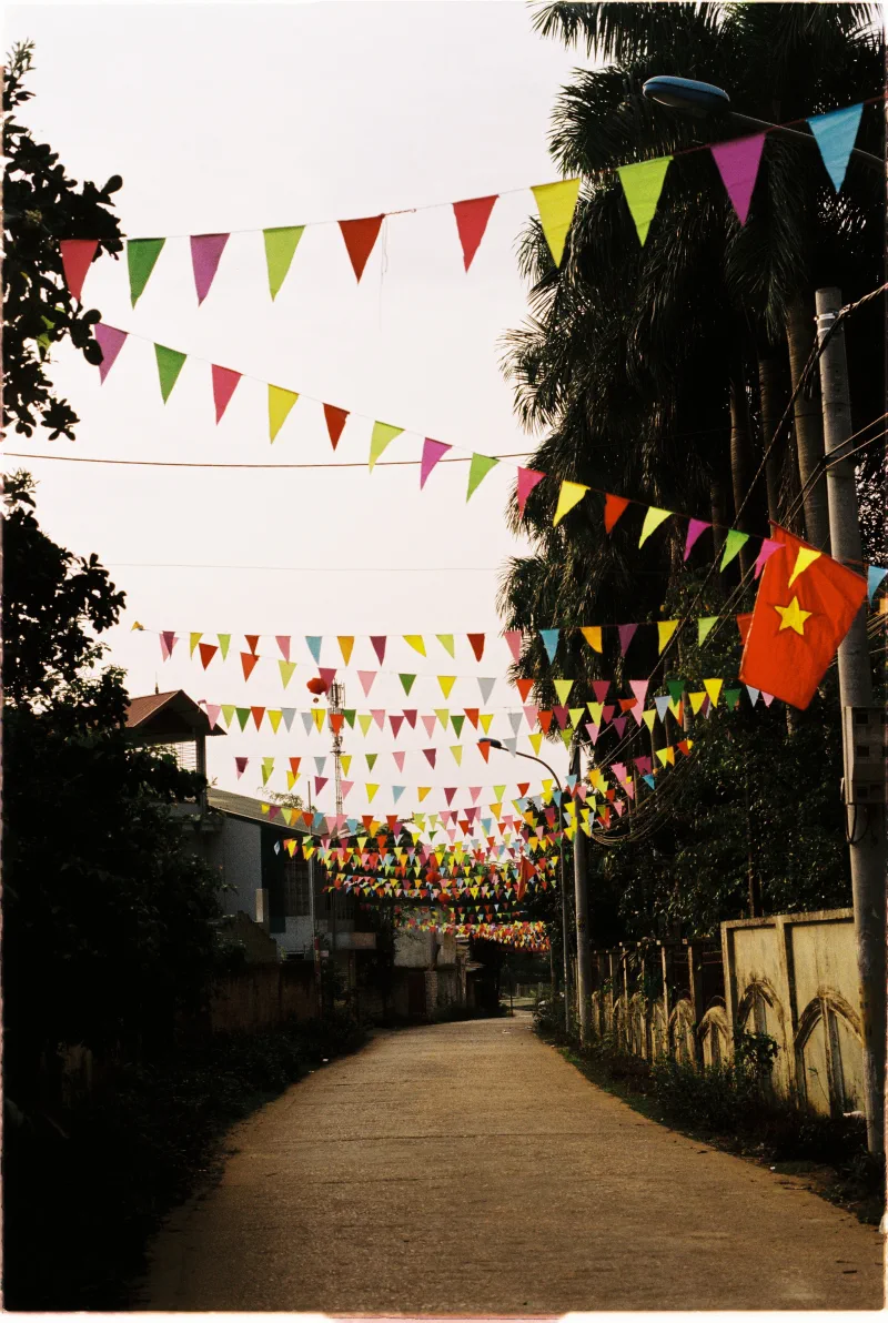 Rows of colourful triangular bunting and a Vietnamese flag recede down an empty lane