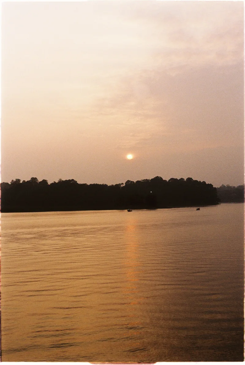 A hazy low sun lays a narrow gold reflection across calm lake water