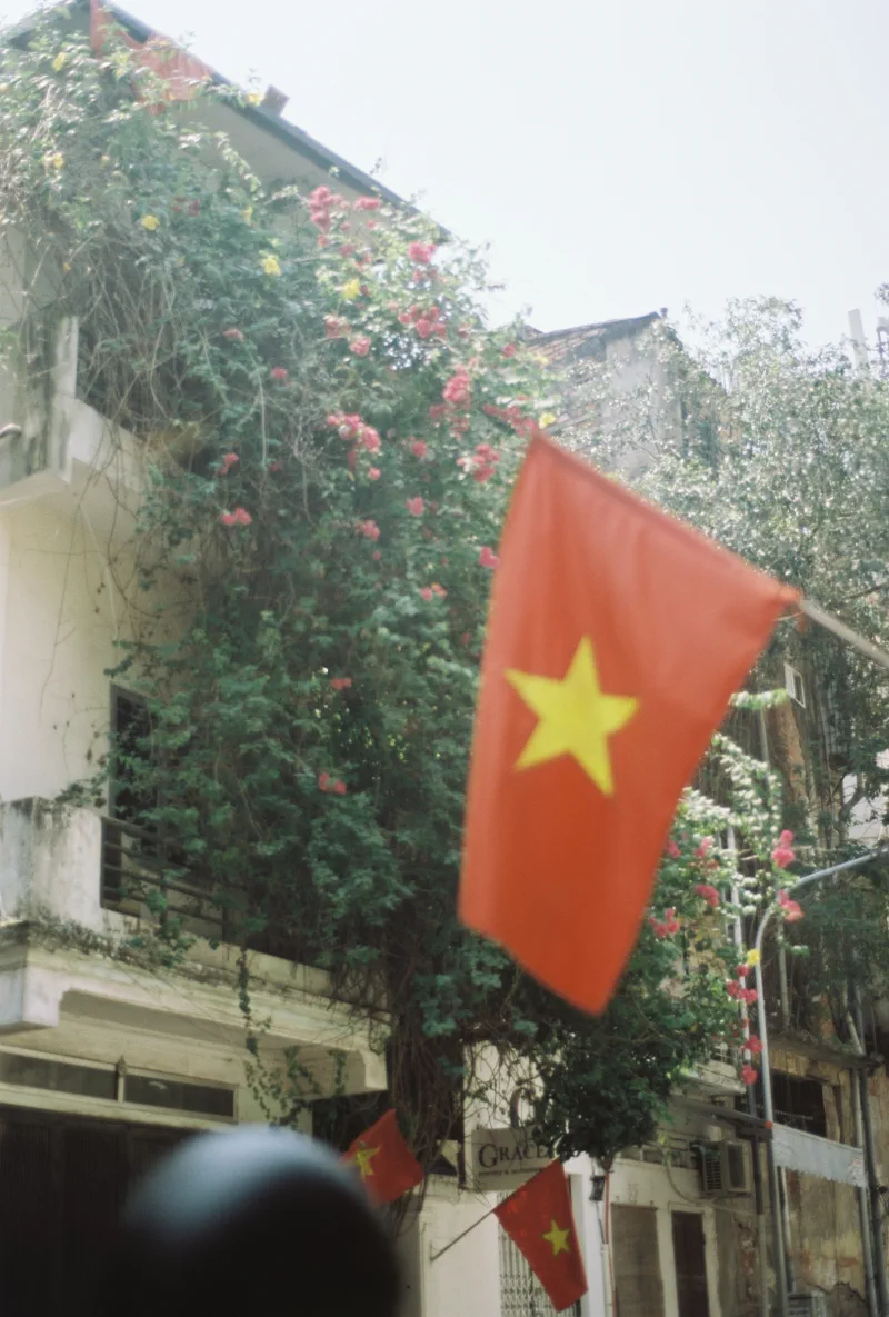 A softly focused Vietnamese flag floats before an old flower-covered facade
