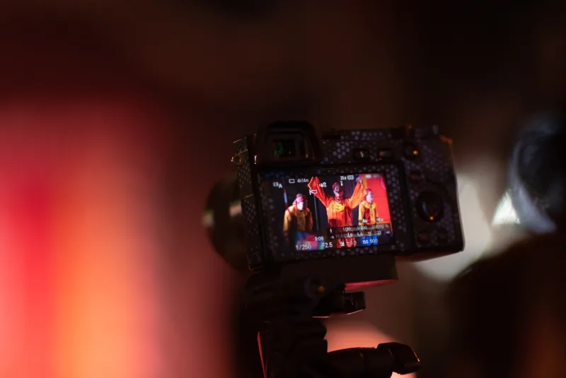 A camera screen shows a red-costumed tuồng performer, surrounded by soft red and black foreground shapes