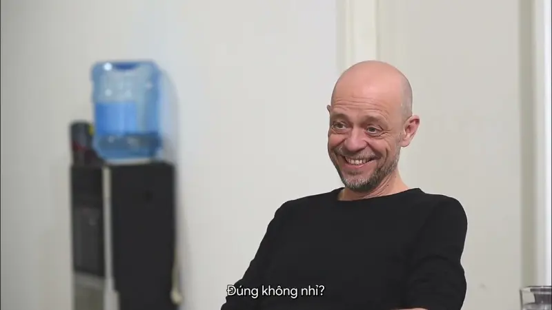 A subtitled interview subject smiles mid-answer in a plain white room